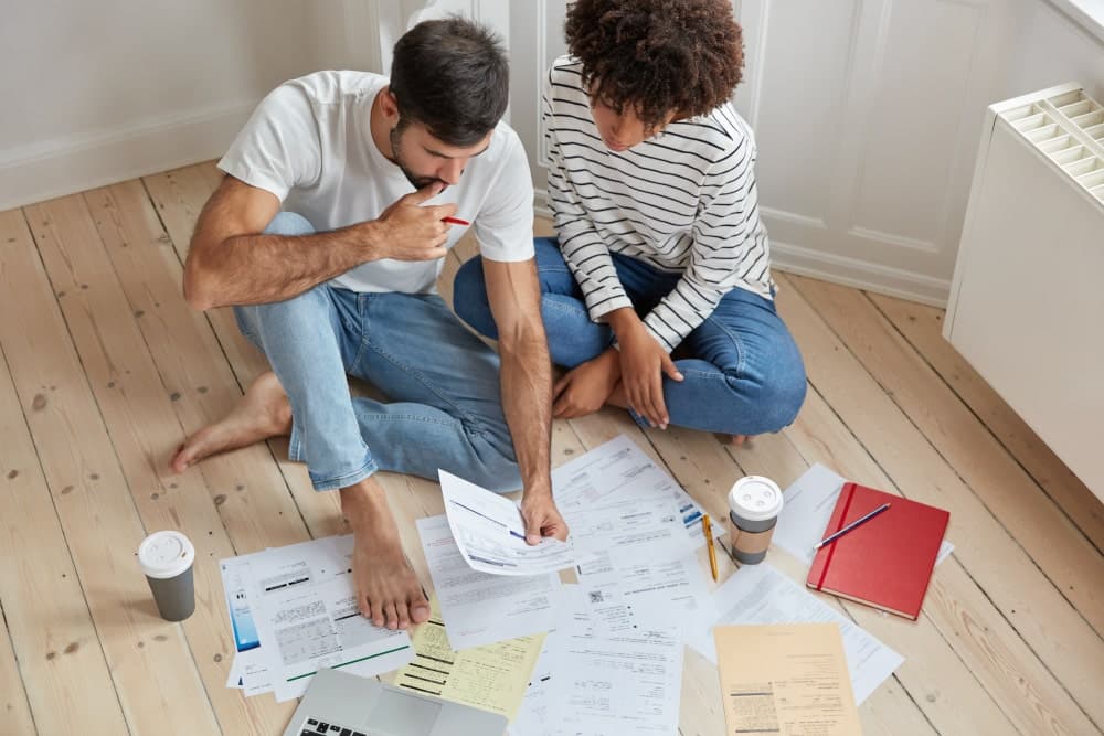 Young couple sitting on the floor of their home with planning documents spread out in front of them